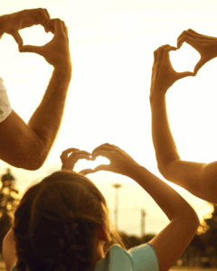 Familie zeigt Herz mit Hand in den Sonnenuntergang
